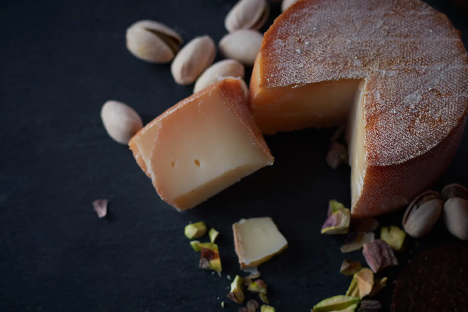 Une meule de fromage affiné entamée, des pistaches autour