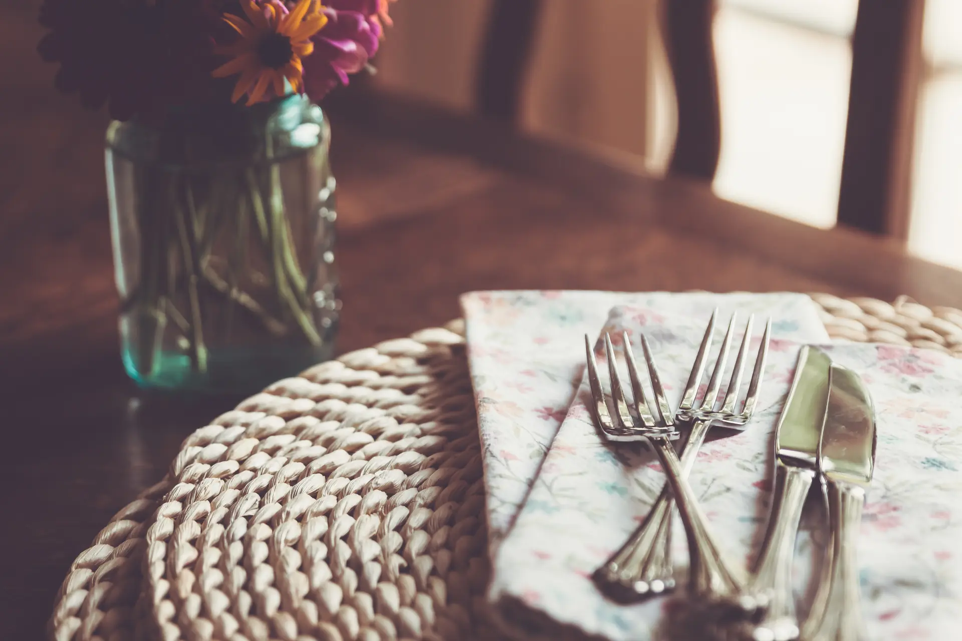 Un couvert dressé sur la table de bois, un pot de fleurs près de la fenêtre