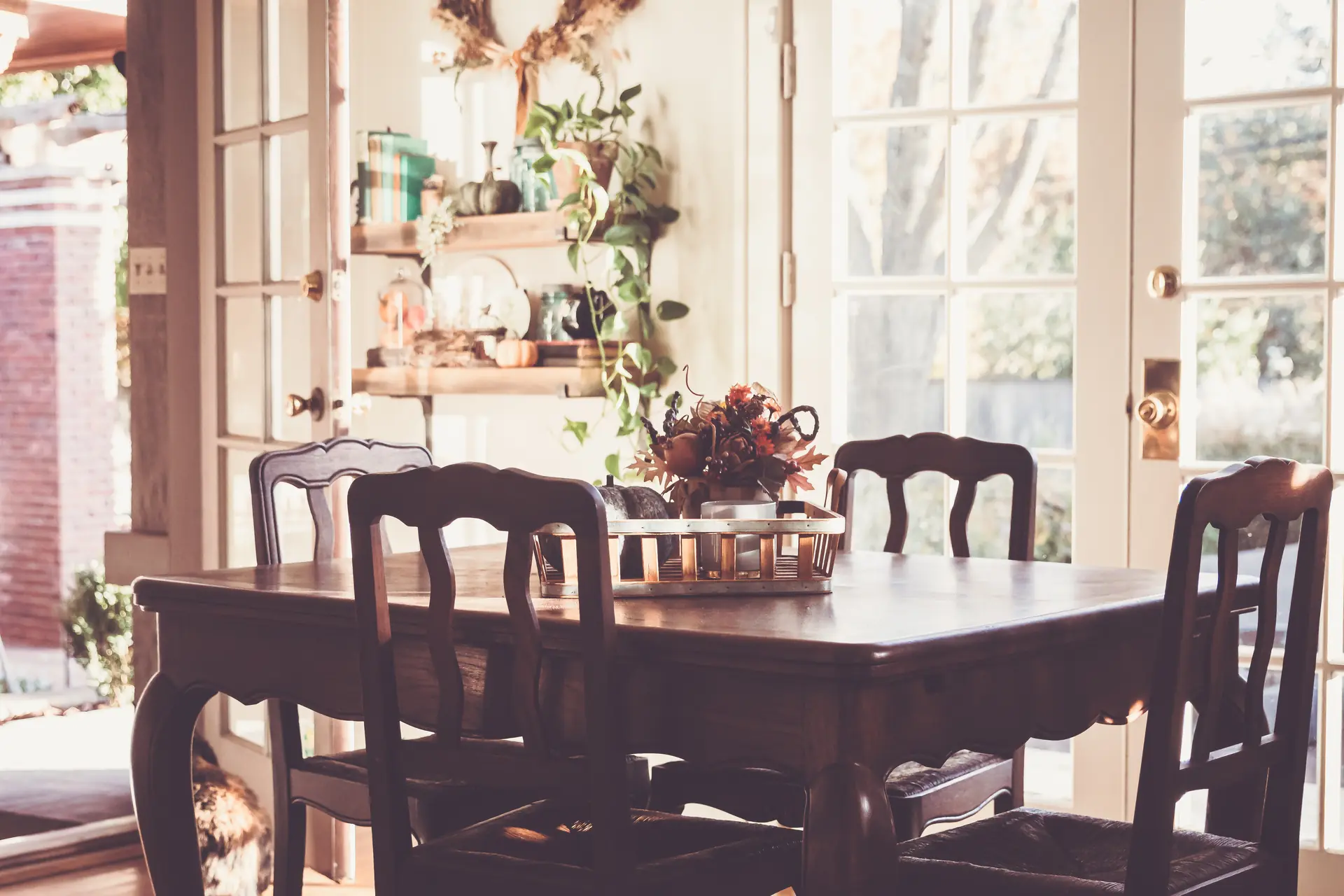 La salle à manger le matin : la table de bois sombre, les chaises sculptées, les portes-fenêtres ouvertes